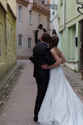 Brudpar fotograferas på smal gata med byggnader i pastellfärger