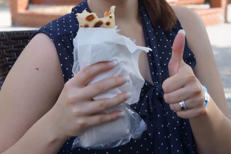 Kvinna hållandes i en kebabrulle med ena handen och gör tummen upp med andra handen