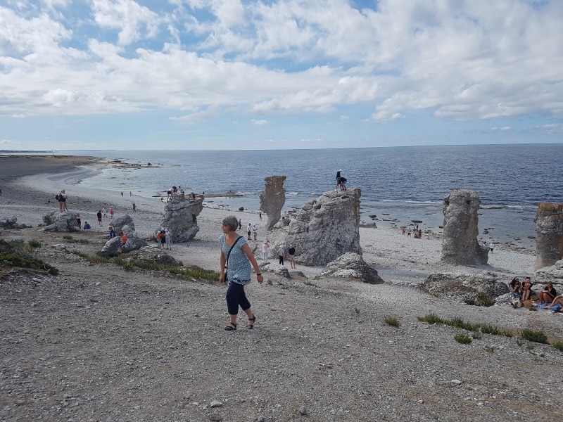 En kvinna går längs raukarna på en stenstrand vid Östersjön