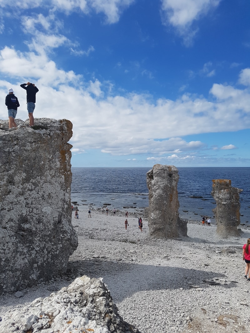 Tre raukar på en stenstrand vid Östersjön. Två personer står uppe på en rauk.