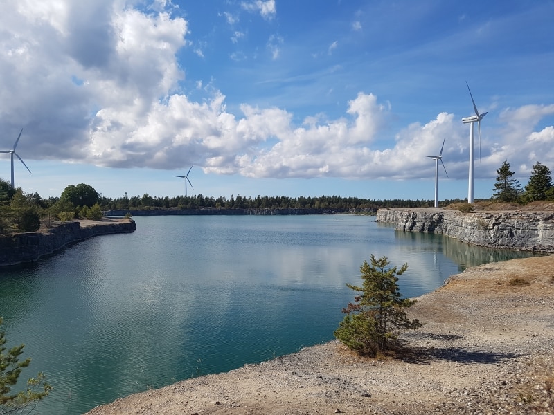 Ett kalkbrott med blått vatten och fyra vindkraftverk i bakgrunden