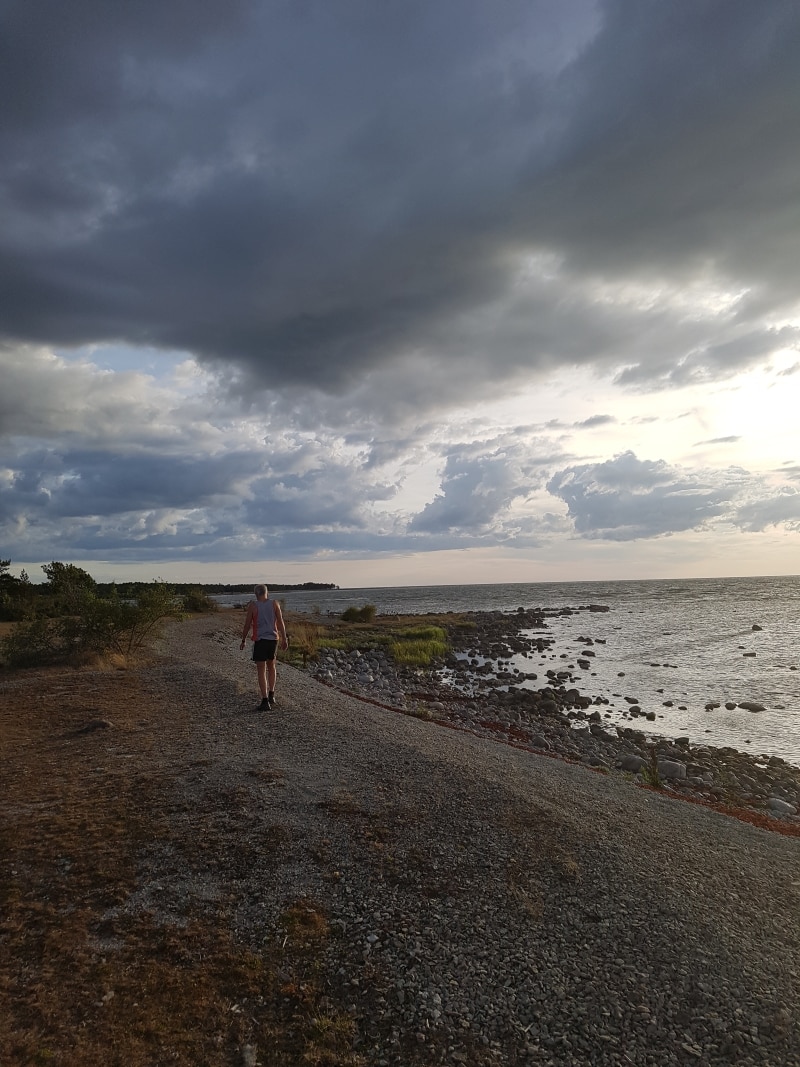 En man går på stenstranden längs havet