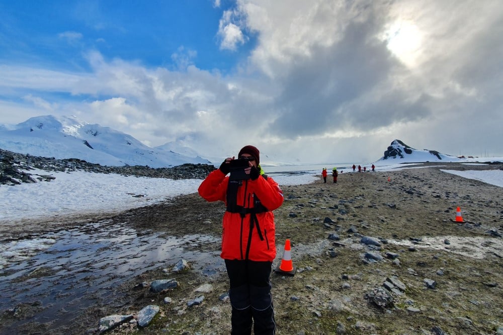 Man fotar på land med snötäckta berg i bakgrunden