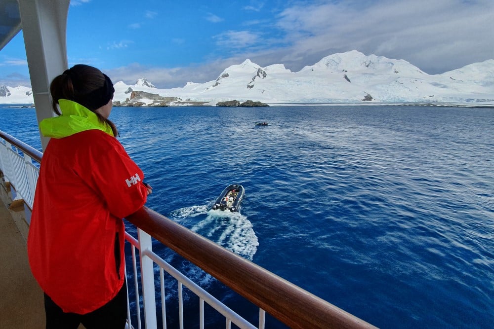 Kvinna på fartyg blickar ut över antarktiska oceanen och snötäckta berg