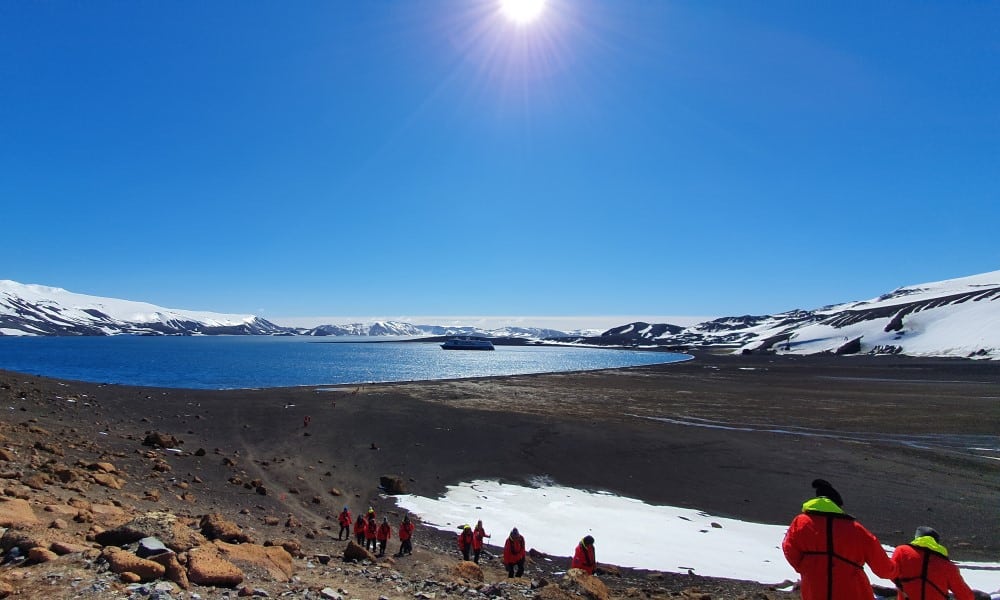 Utsikt från kulle över land med lite snö, antarktiska oceanen och snötäckta berg