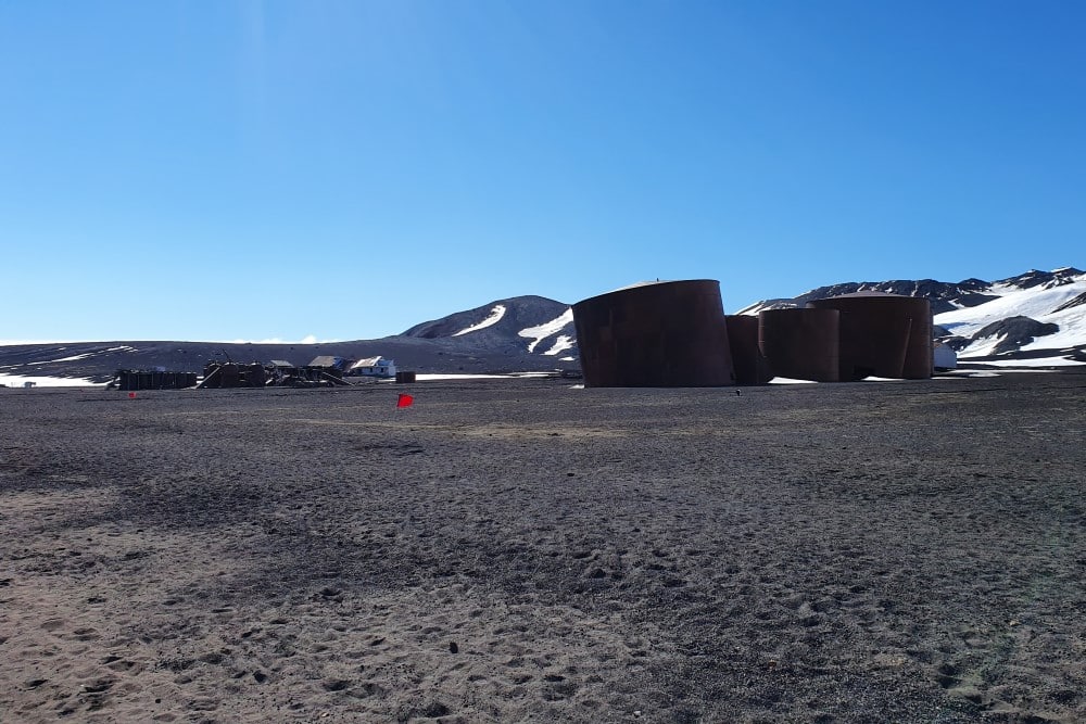 Gamla byggnader på land framför kullar med lite snö