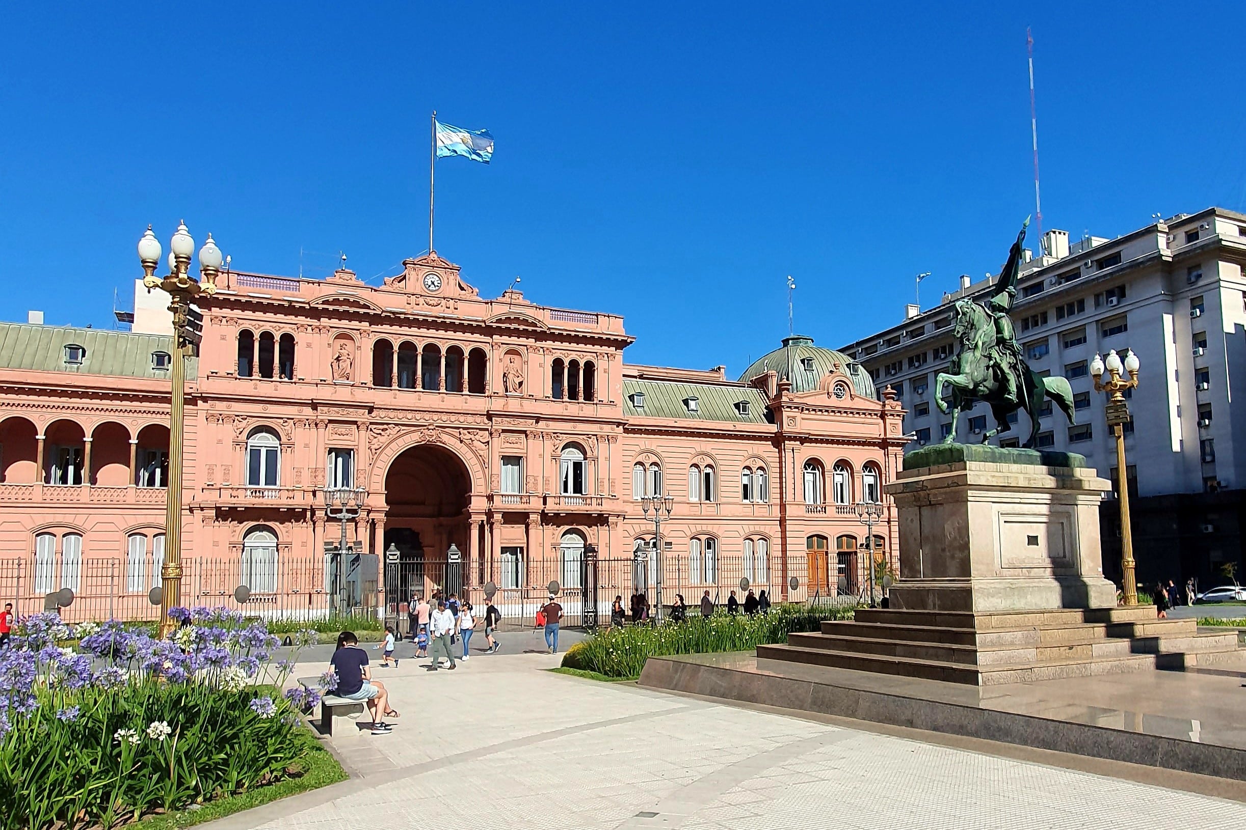 Stor rosa byggnad med grönt tak och en staty med en man på en häst utanför