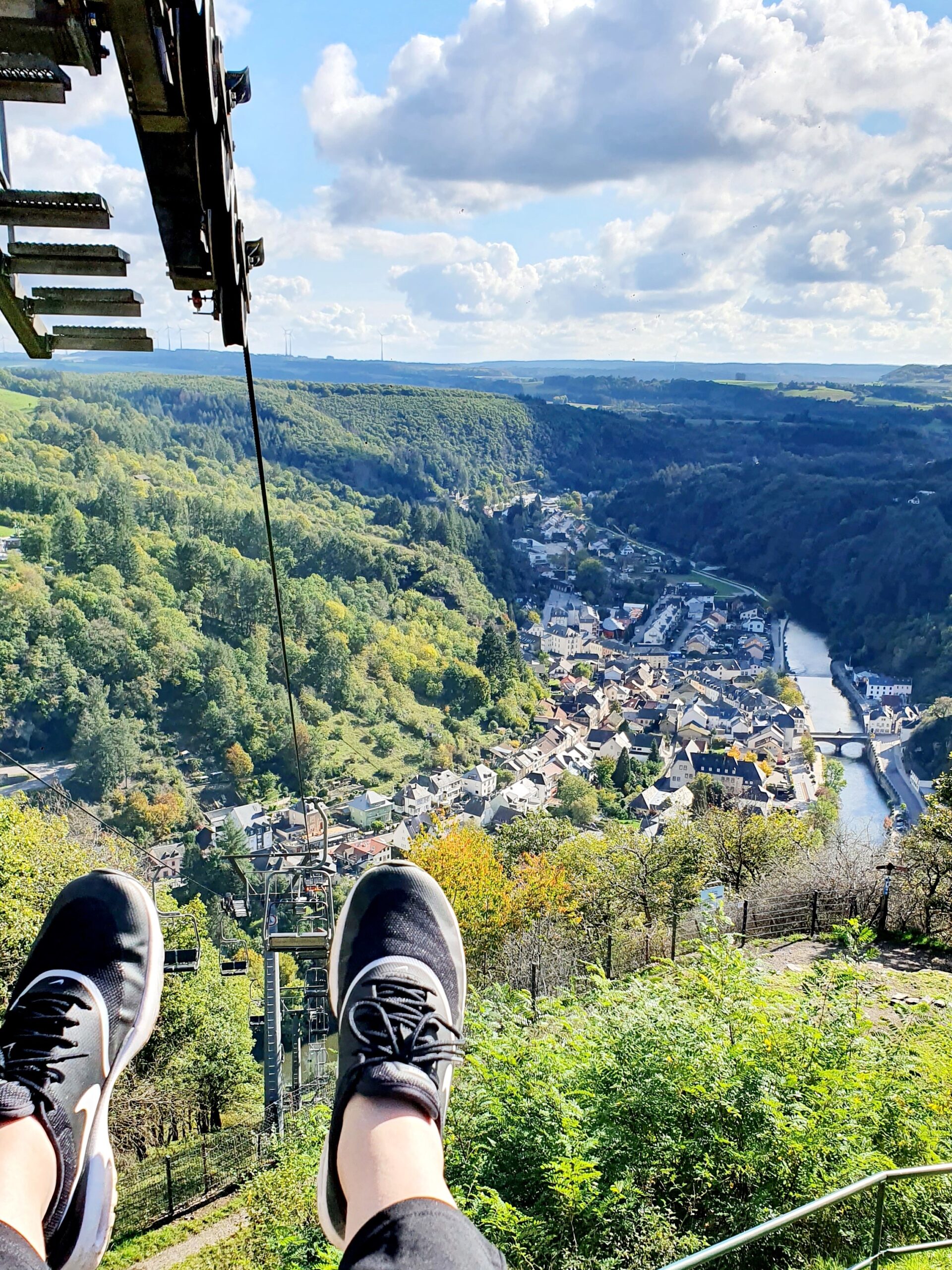 Två fötter dinglar från en lift med utsikt över stad och å