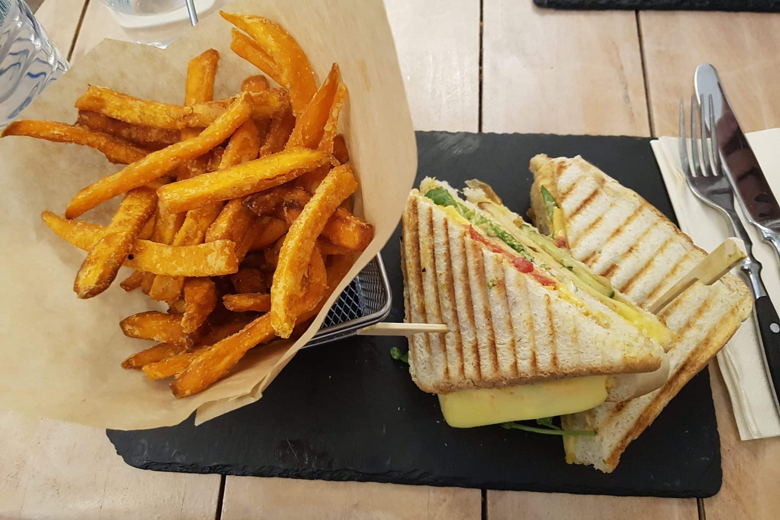 Sötpotatispommes och club sandwich på en svart stenbricka och bestick bredvid