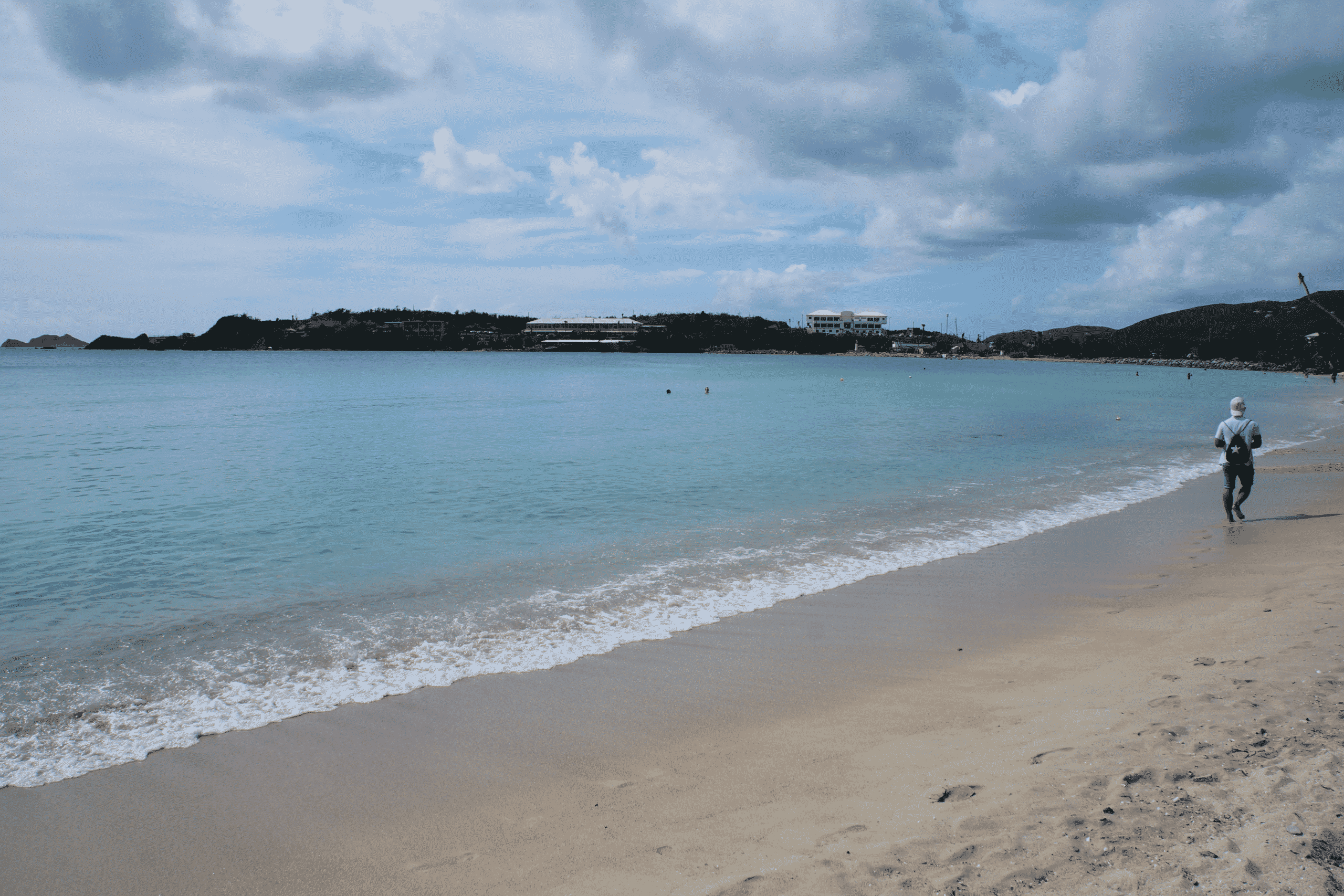 Sandstrand med turkost vatten och några få personer som badar samt en som går längs strandkanten