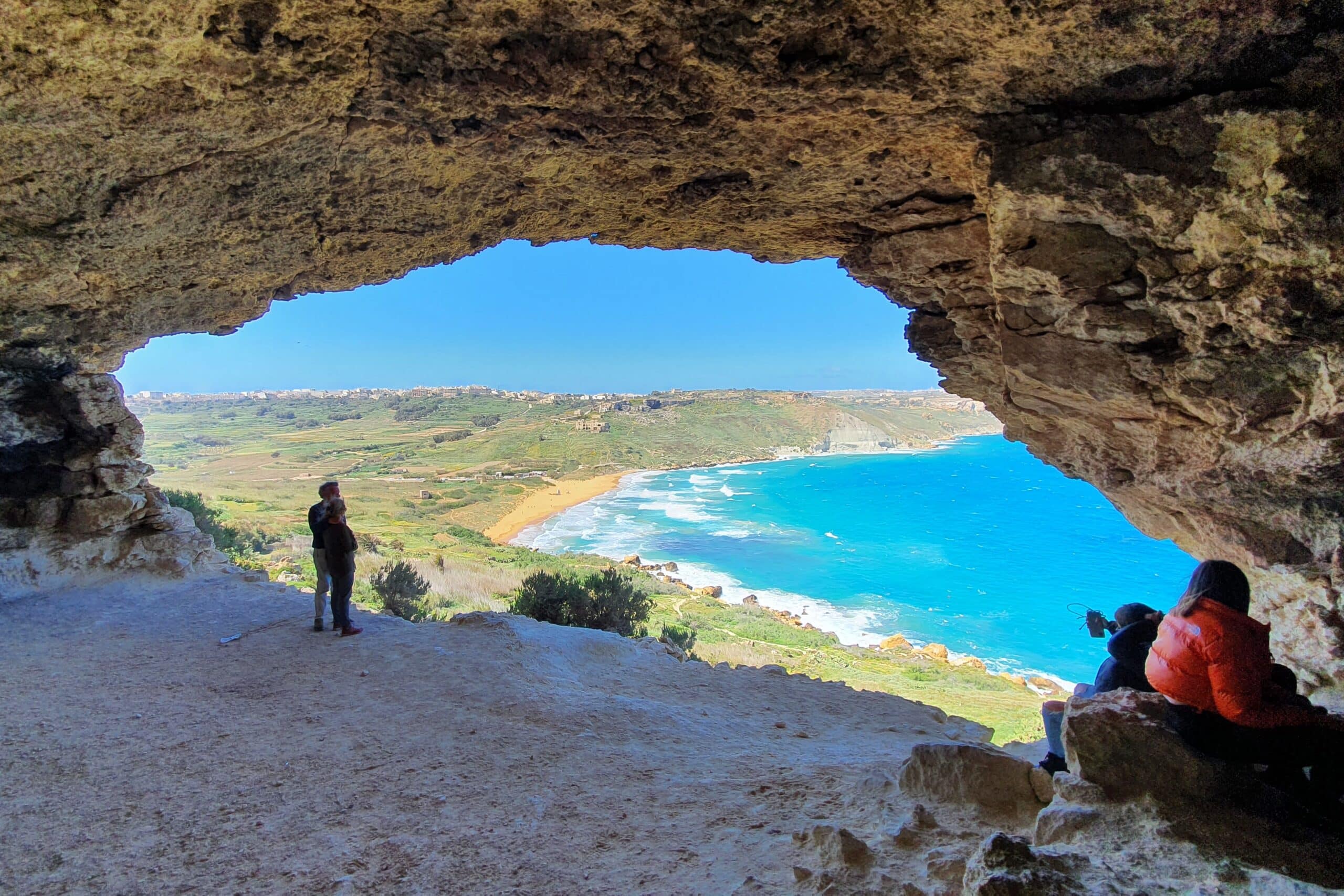 Grotta med stor öppning med utsikt över landskap, strand och blått hav